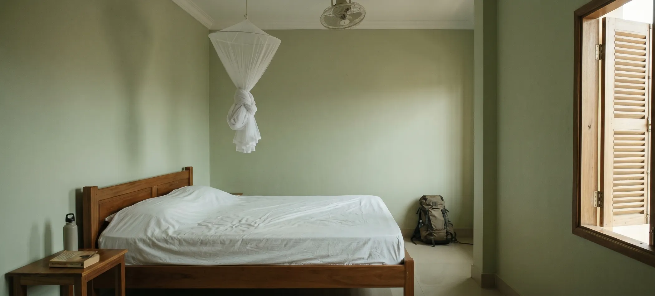 A simply furnished rented room in Kampot - wooden bed, mosquito net, louvred shutters open to morning light